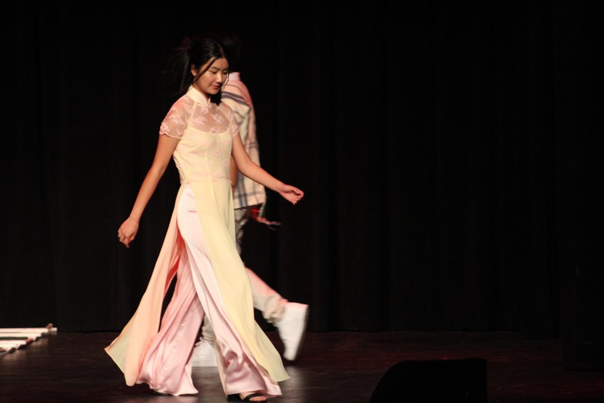 Junior Sarah Ho modeling a yellow Áo dài with pink lace flowers on it.
